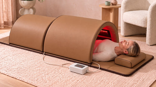 The Restore Dome™ full-body infrared sauna in caramel, in a bright living room, with a woman lying inside and her head resting outside
