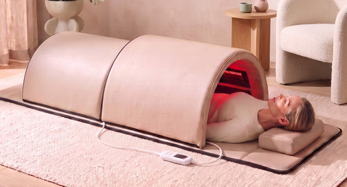 The Restore Dome™ full-body infrared sauna in a bright living room, head resting outside the larger dome section